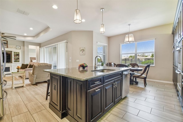 kitchen featuring light stone countertops, a kitchen bar, sink, decorative light fixtures, and a center island with sink