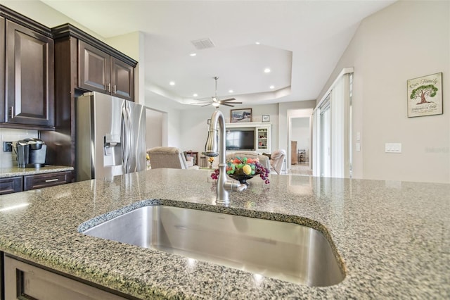 kitchen featuring stone counters, sink, ceiling fan, stainless steel fridge, and dark brown cabinets