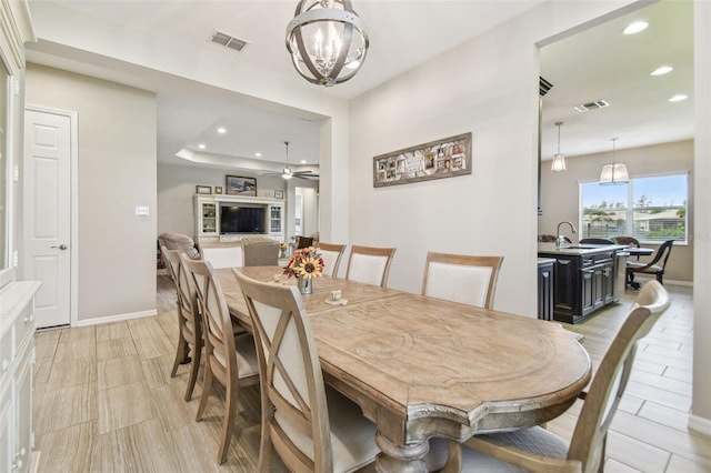 dining space with a tray ceiling, sink, and ceiling fan with notable chandelier