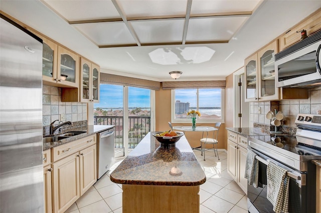 kitchen with backsplash, sink, dark stone countertops, appliances with stainless steel finishes, and light tile patterned flooring