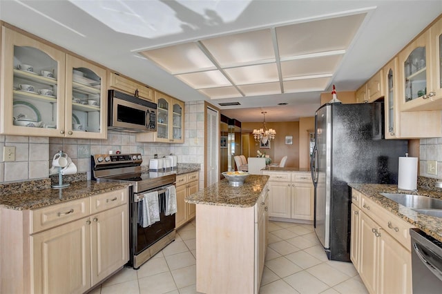 kitchen with light stone countertops, an inviting chandelier, tasteful backsplash, a kitchen island, and appliances with stainless steel finishes