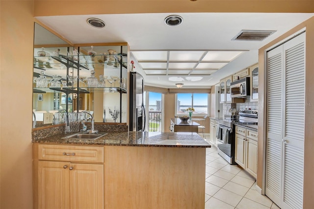 kitchen featuring dark stone counters, sink, light tile patterned floors, kitchen peninsula, and stainless steel appliances