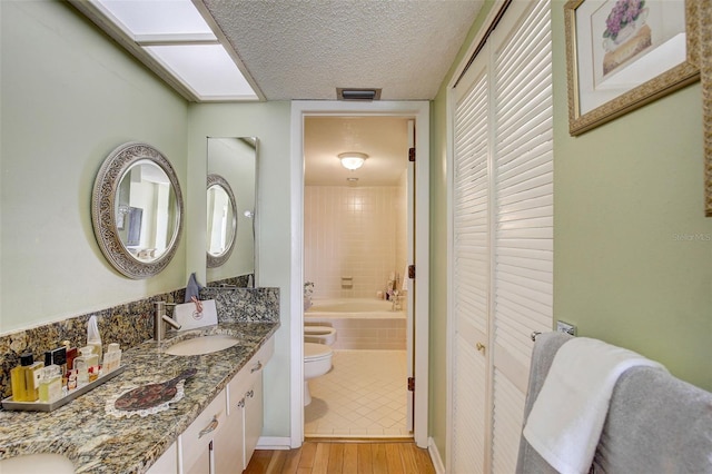 full bathroom featuring wood-type flooring, a textured ceiling, toilet, vanity, and tiled shower / bath