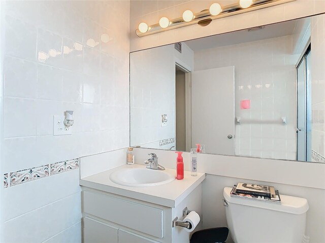 bathroom featuring vanity, a shower with door, toilet, and tile walls