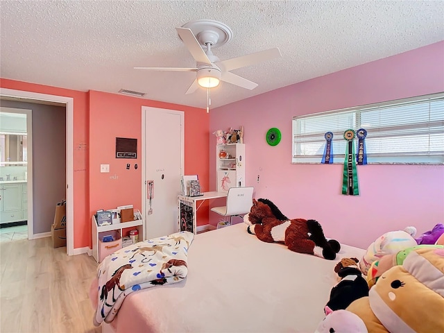 bedroom featuring ceiling fan, ensuite bath, a textured ceiling, and light hardwood / wood-style flooring