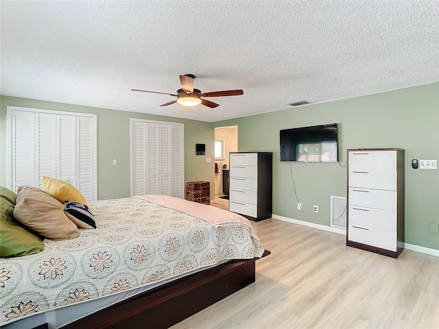 bedroom with a textured ceiling, two closets, light hardwood / wood-style flooring, and ceiling fan