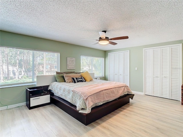 bedroom with ceiling fan, light wood-type flooring, a textured ceiling, and multiple closets