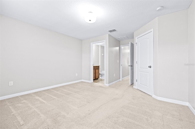 unfurnished bedroom featuring connected bathroom, light carpet, and a textured ceiling