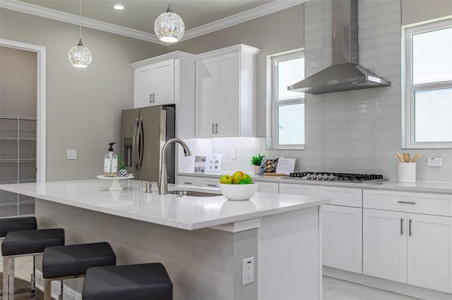 kitchen featuring wall chimney range hood, sink, stainless steel appliances, and white cabinets