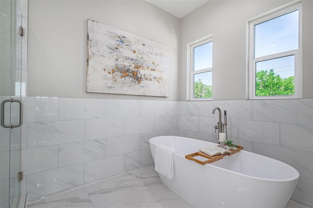 bathroom with tile walls, a wealth of natural light, and separate shower and tub