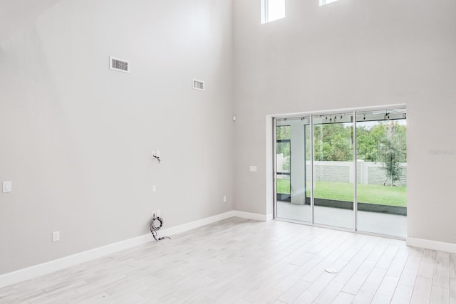 empty room featuring a high ceiling, light wood-type flooring, and plenty of natural light