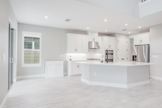 kitchen with stainless steel appliances, a center island with sink, white cabinetry, and light hardwood / wood-style flooring