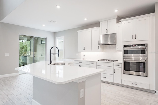 kitchen featuring stainless steel appliances, white cabinetry, sink, a kitchen island with sink, and light hardwood / wood-style flooring