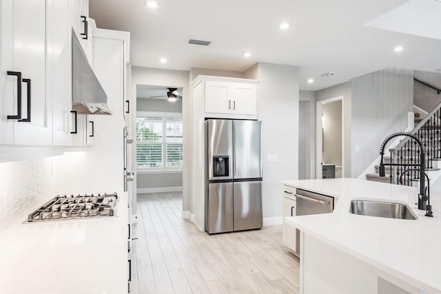 kitchen with light hardwood / wood-style floors, white cabinetry, sink, extractor fan, and appliances with stainless steel finishes