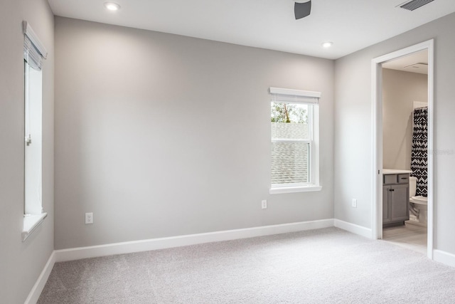 unfurnished bedroom with ceiling fan, light colored carpet, and ensuite bath