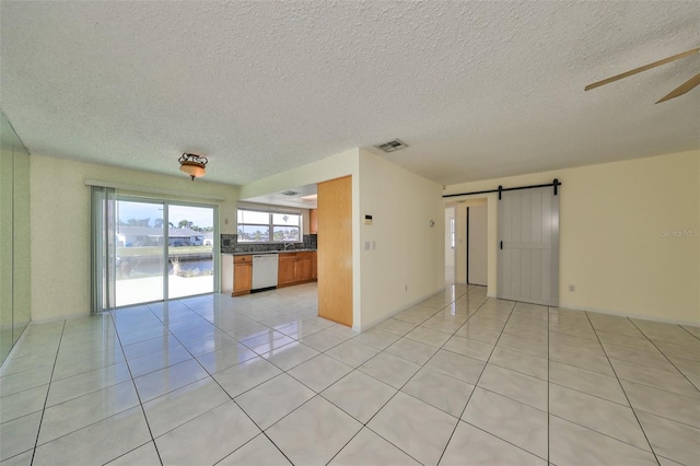 unfurnished room with a textured ceiling, a barn door, a water view, and light tile patterned floors