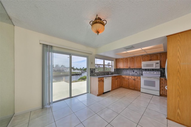 kitchen featuring tasteful backsplash, a water view, light tile patterned flooring, and white appliances