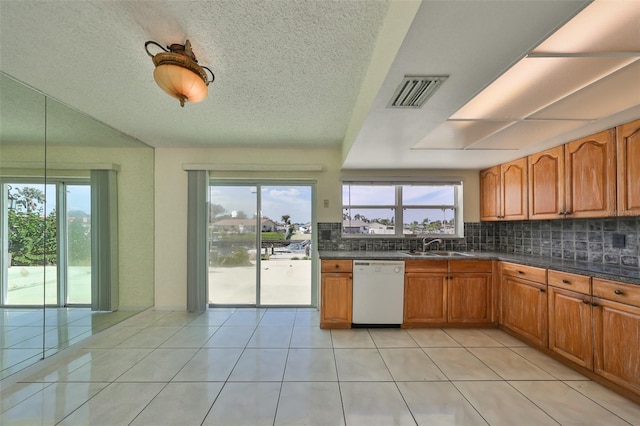 kitchen with light tile patterned floors, a textured ceiling, white dishwasher, and tasteful backsplash