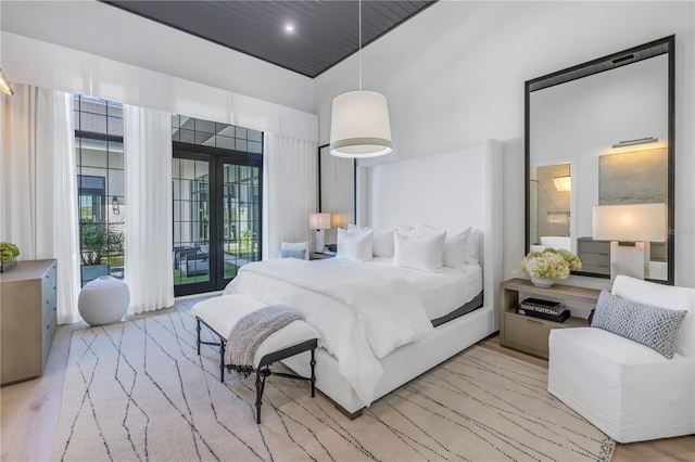 bedroom featuring access to exterior, french doors, a towering ceiling, and light hardwood / wood-style floors