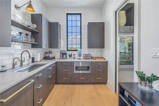 kitchen with decorative backsplash, dark brown cabinetry, sink, and light hardwood / wood-style flooring