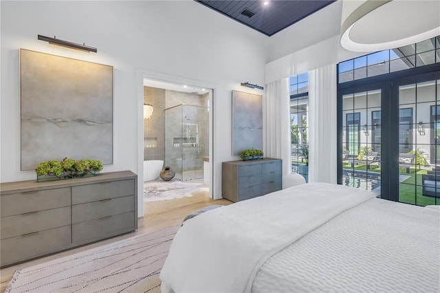 bedroom with ensuite bath, light wood-style flooring, and a towering ceiling