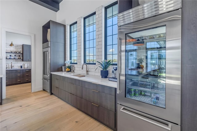 kitchen featuring wine cooler, light wood finished floors, open shelves, light countertops, and a sink