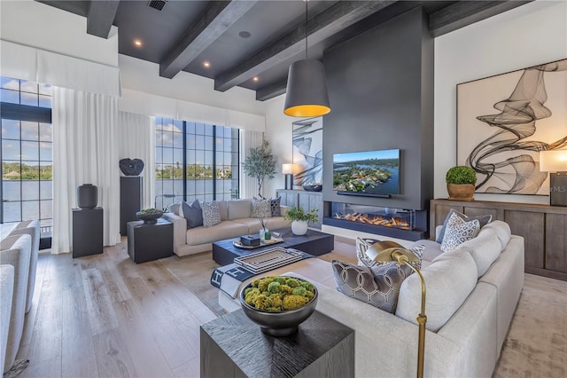 living area with a towering ceiling, light wood finished floors, beam ceiling, and a glass covered fireplace