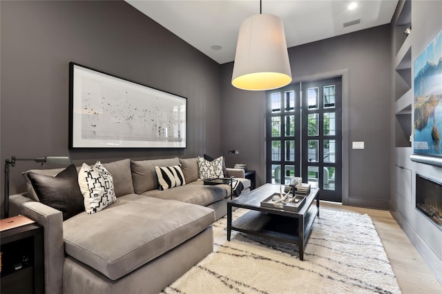 living room with a glass covered fireplace, visible vents, light wood-style flooring, and baseboards