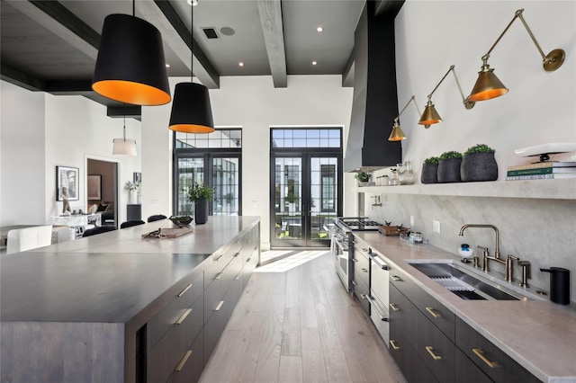 kitchen with light wood-style flooring, island range hood, a sink, stainless steel range, and pendant lighting