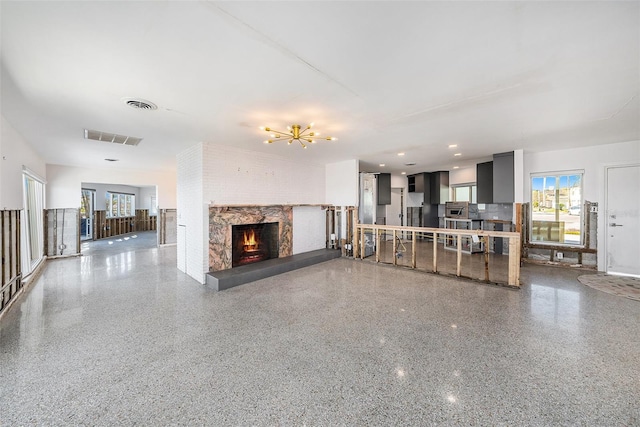 unfurnished living room with an inviting chandelier and a brick fireplace