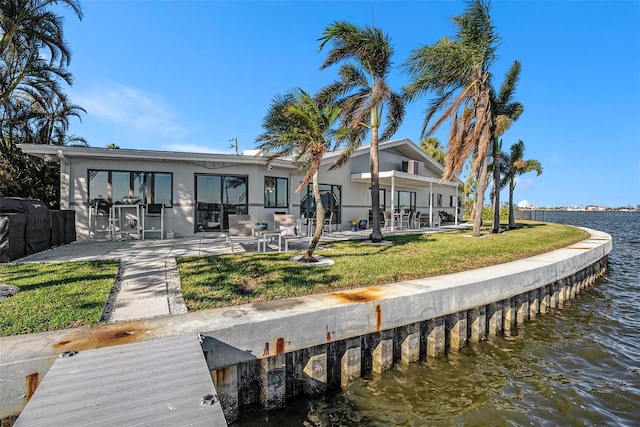 back of property with a lawn, a patio area, and a water view