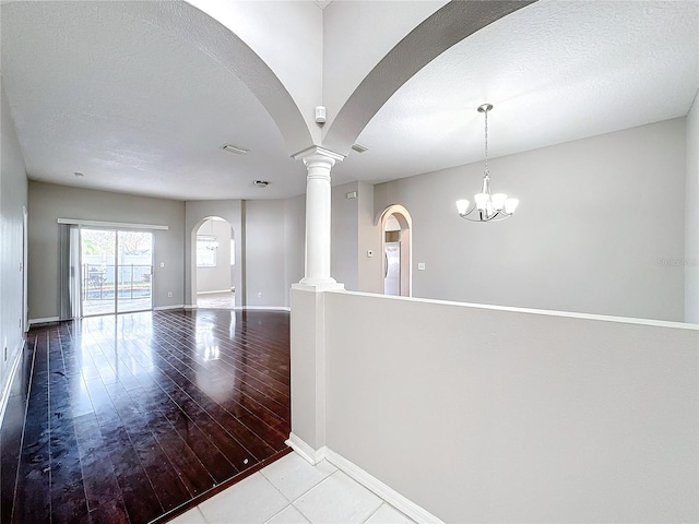 spare room featuring a chandelier, wood-type flooring, ornate columns, and a textured ceiling