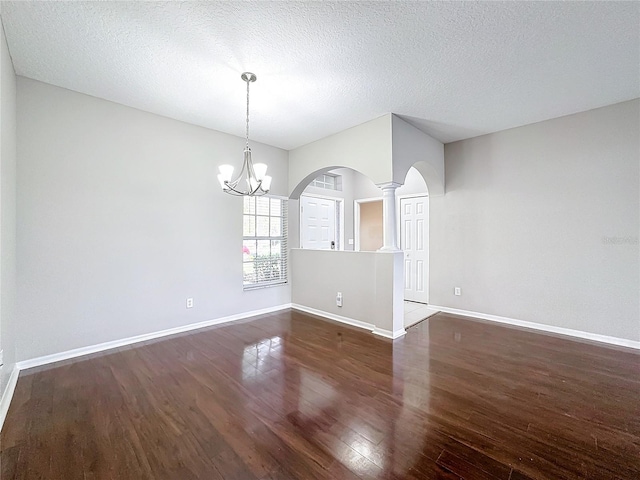 empty room with dark wood-type flooring, a textured ceiling, and ornate columns