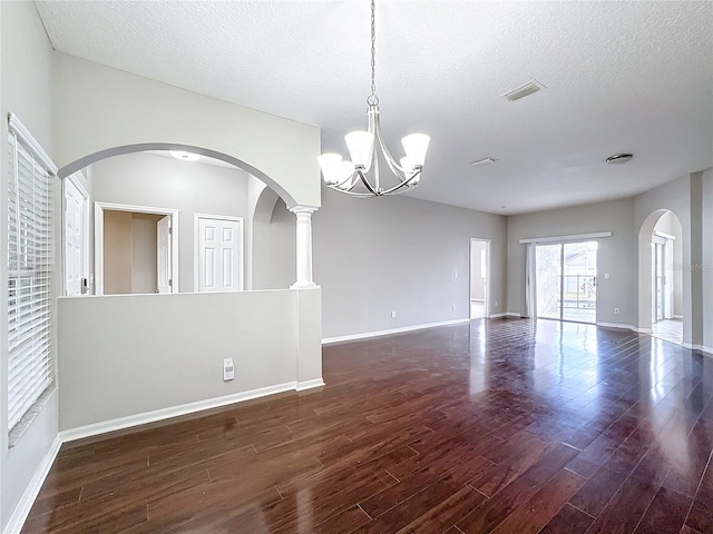 unfurnished room with a textured ceiling, an inviting chandelier, dark hardwood / wood-style flooring, and decorative columns