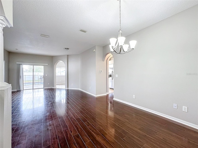 empty room featuring dark wood-type flooring, an inviting chandelier, and a textured ceiling