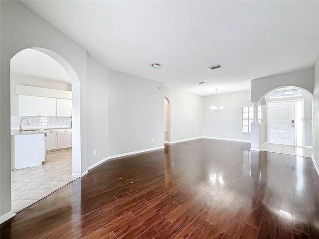 unfurnished living room featuring sink, an inviting chandelier, and wood-type flooring