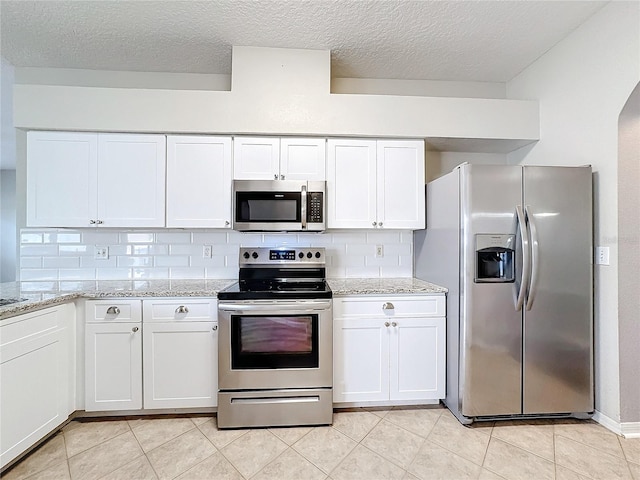 kitchen featuring light stone countertops, appliances with stainless steel finishes, decorative backsplash, and white cabinets