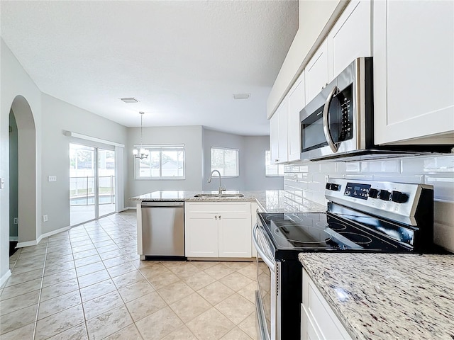 kitchen featuring kitchen peninsula, sink, light stone countertops, white cabinetry, and appliances with stainless steel finishes