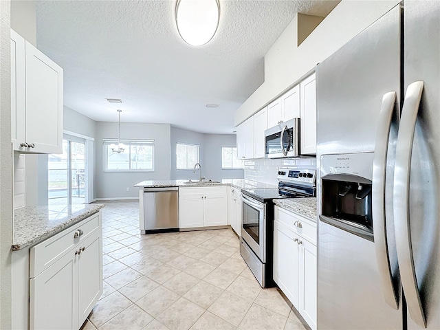 kitchen with stainless steel appliances, white cabinets, kitchen peninsula, light stone countertops, and pendant lighting