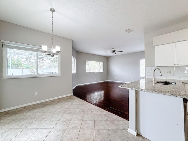 kitchen with light hardwood / wood-style floors, white cabinetry, sink, light stone countertops, and decorative light fixtures