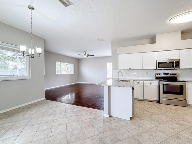 kitchen featuring stainless steel appliances, light stone counters, hanging light fixtures, sink, and white cabinetry