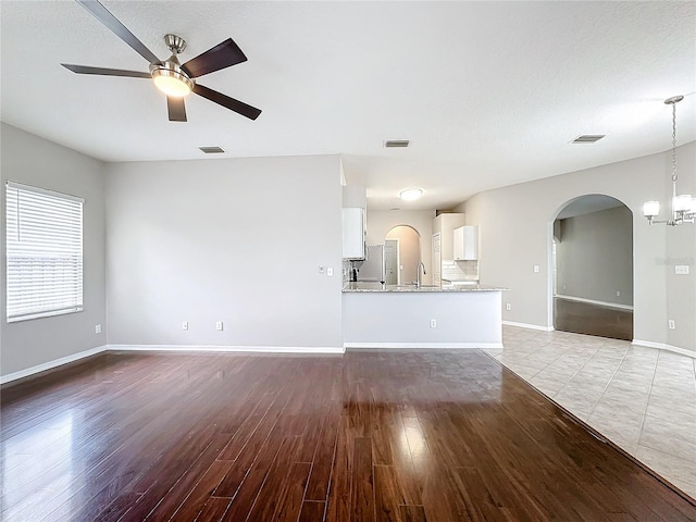 unfurnished living room featuring ceiling fan with notable chandelier and light hardwood / wood-style floors