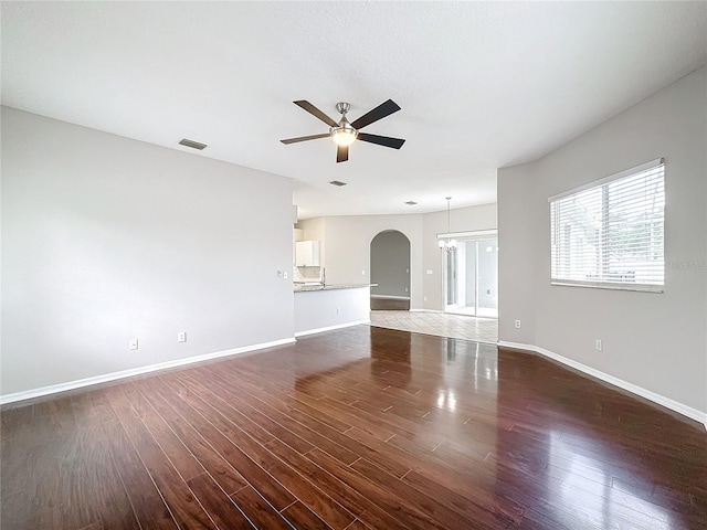 unfurnished living room featuring ceiling fan with notable chandelier and dark hardwood / wood-style flooring