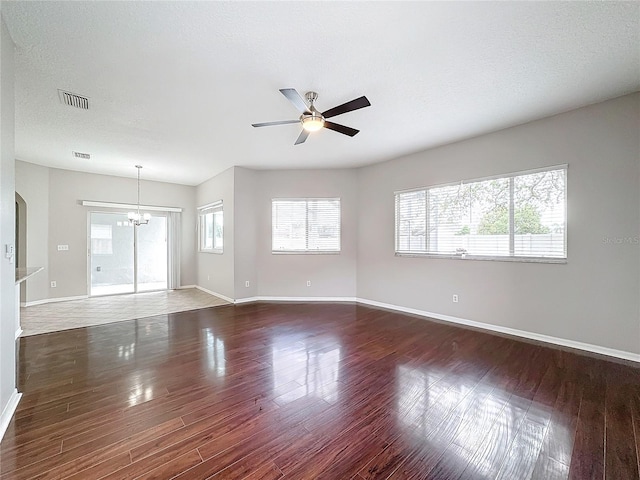 empty room featuring ceiling fan with notable chandelier, dark wood-type flooring, and a textured ceiling