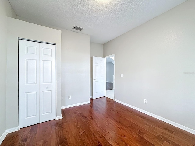 unfurnished bedroom featuring a textured ceiling, a closet, and dark hardwood / wood-style flooring