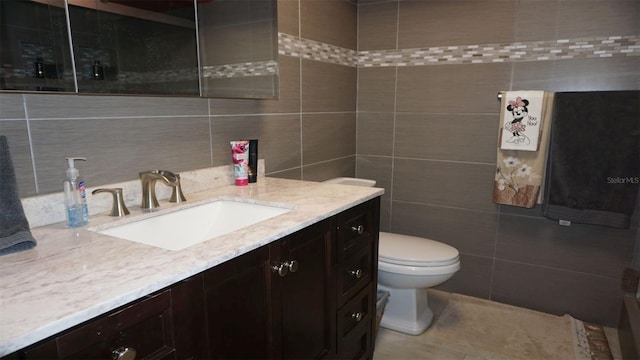 bathroom with toilet, vanity, and tile walls