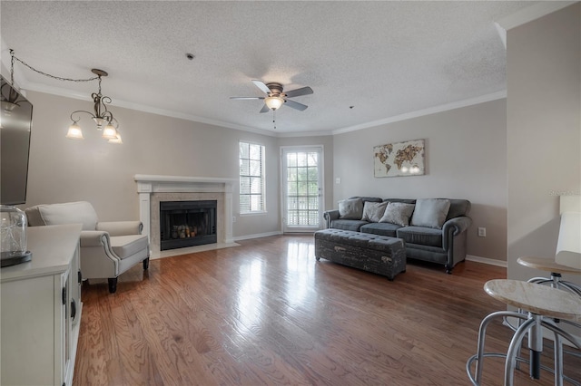 living room with ceiling fan with notable chandelier, wood-type flooring, a textured ceiling, and ornamental molding