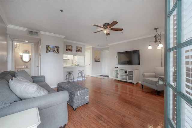 living room with ceiling fan with notable chandelier, sink, hardwood / wood-style flooring, ornamental molding, and a textured ceiling