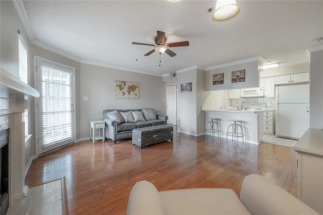 living room featuring crown molding, ceiling fan, a textured ceiling, and light wood-type flooring