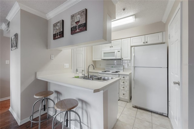 kitchen featuring kitchen peninsula, a kitchen breakfast bar, white appliances, a textured ceiling, and white cabinets